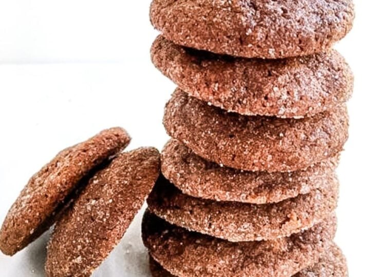 A stack of round, sugar-coated chocolate cinnamon cookies with two cookies lying beside the stack.