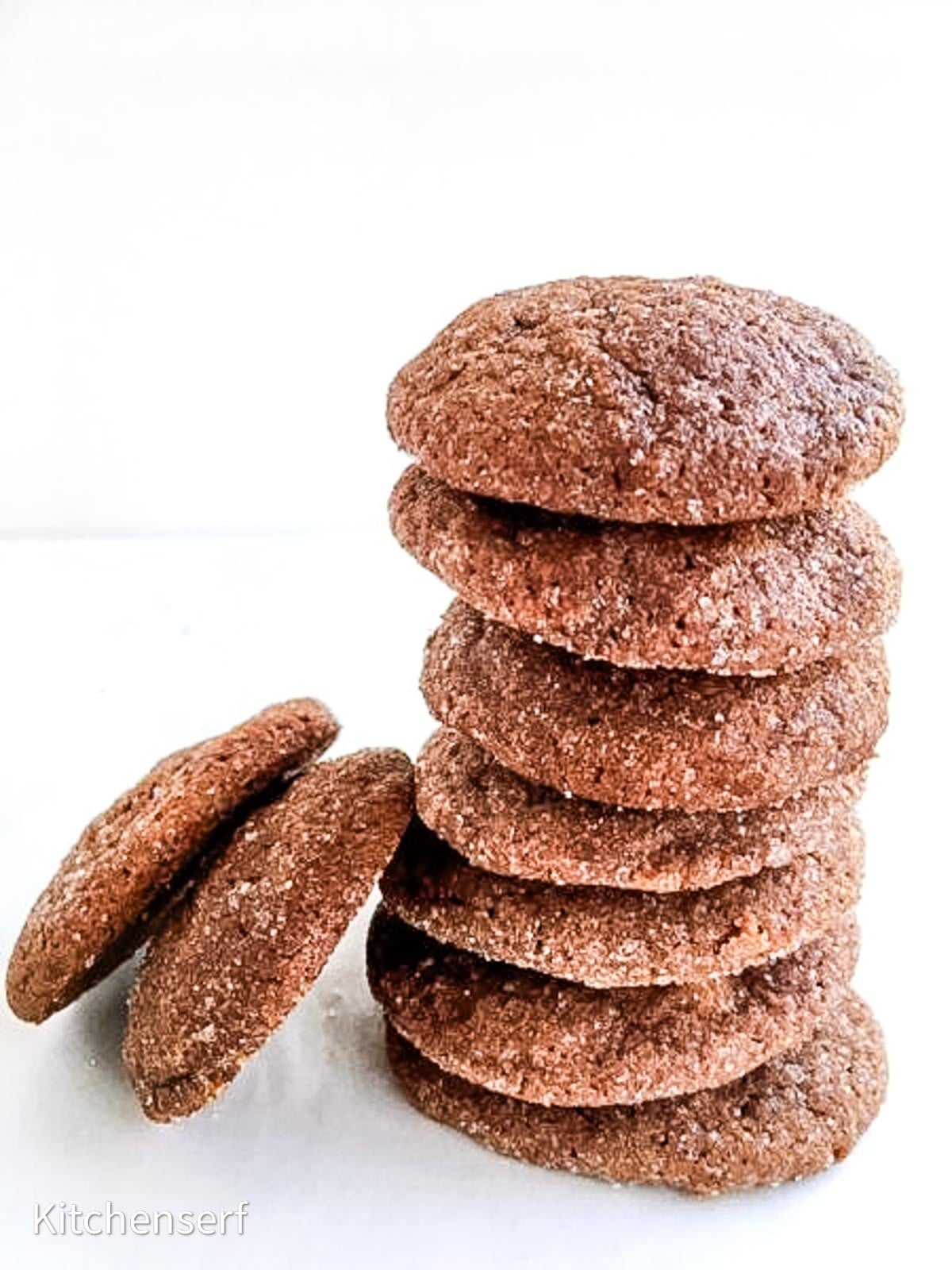 Stack of nine sugar-coated chocolate cinnamon cookies with two leaning on the side, on a white background.