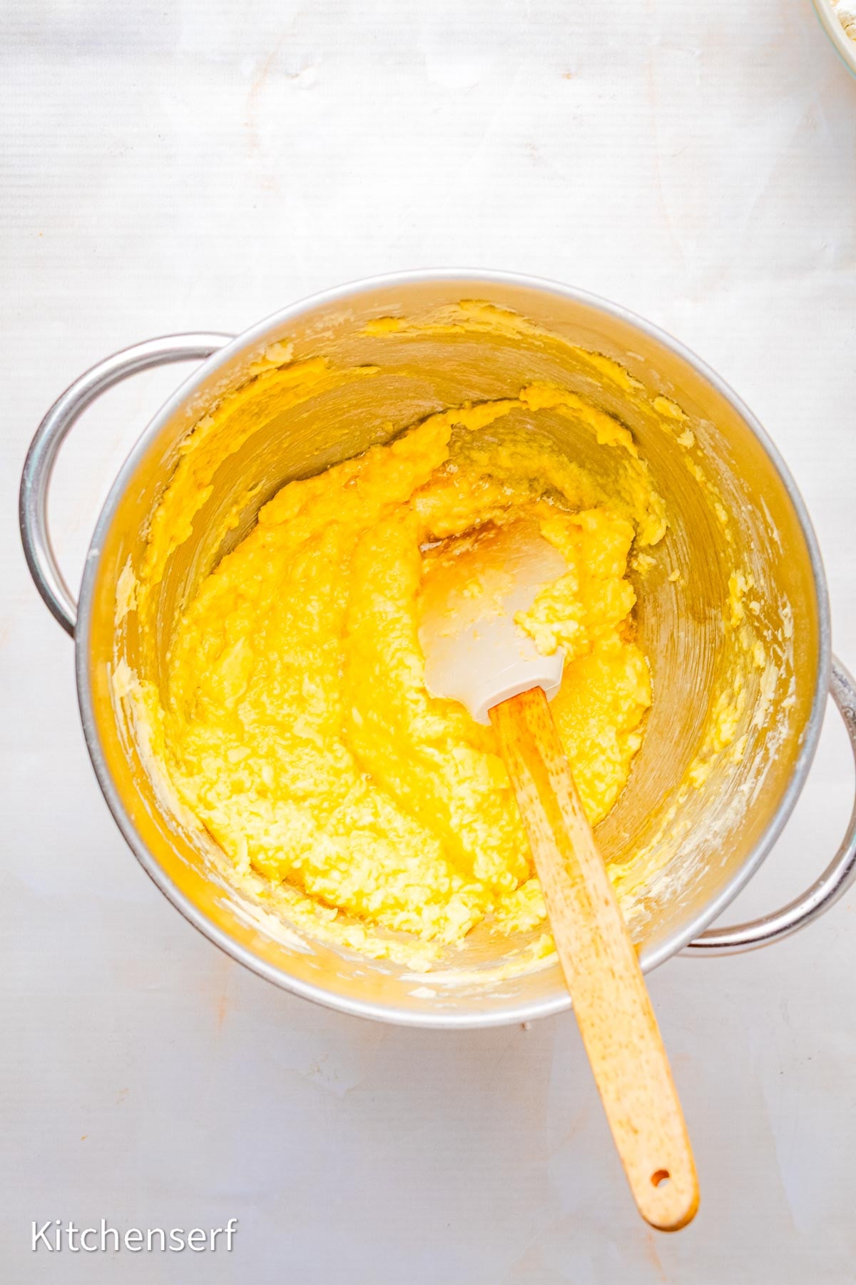 Sugar cookie dough for peppermint pinwheel cookies being mixed in a metal bowl with a spatula on a white surface.