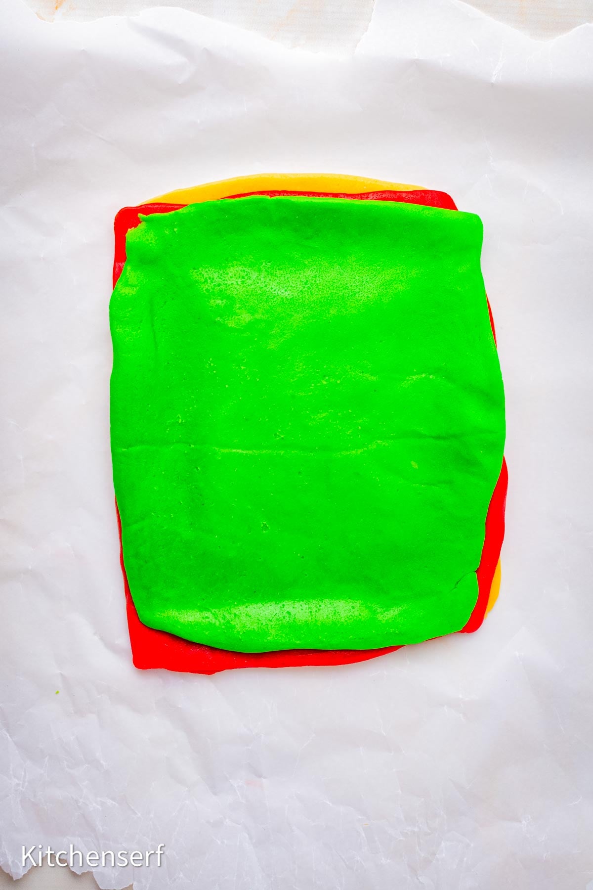 Bright green, red, and plain square layers of sugar cookie dough stacked on white parchment paper.