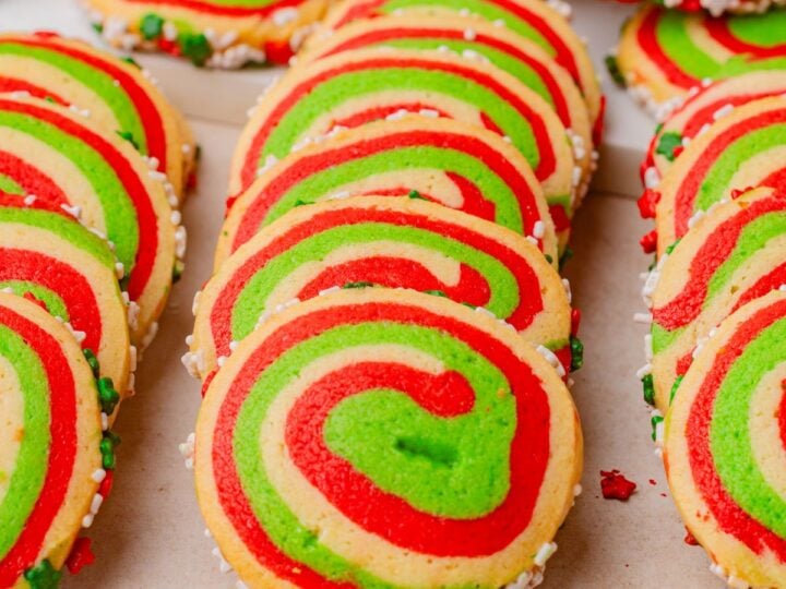Swirled red, green, and whiteish peppermint pinwheel cookies with sprinkles, arranged in rows on a light surface.