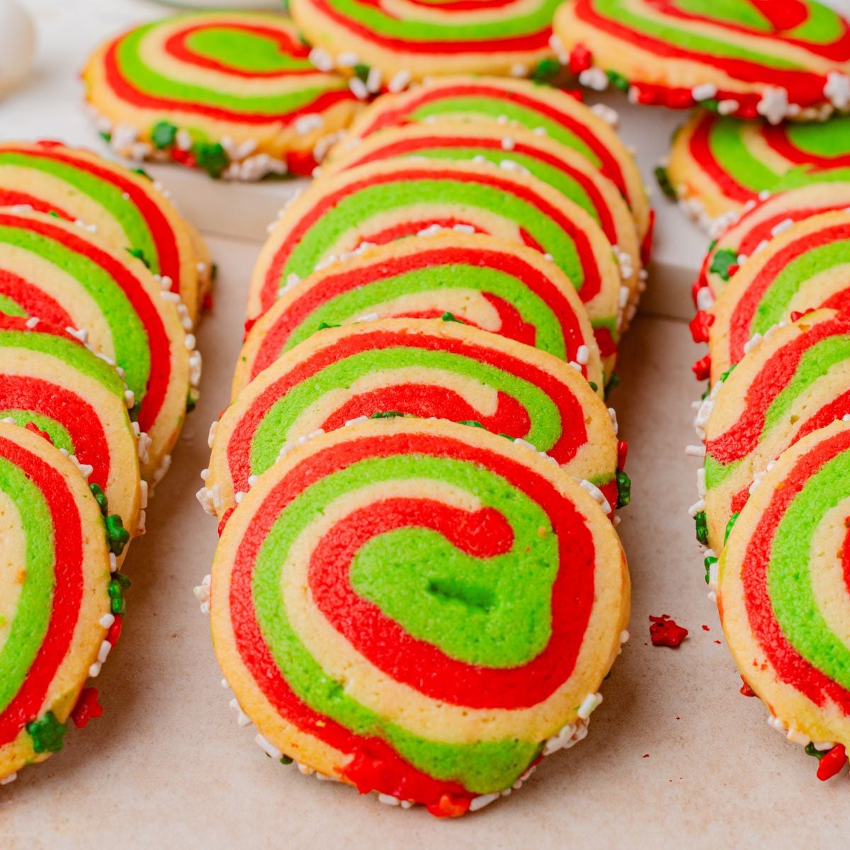Swirled red, green, and whiteish peppermint pinwheel cookies with sprinkles, arranged in rows on a light surface.