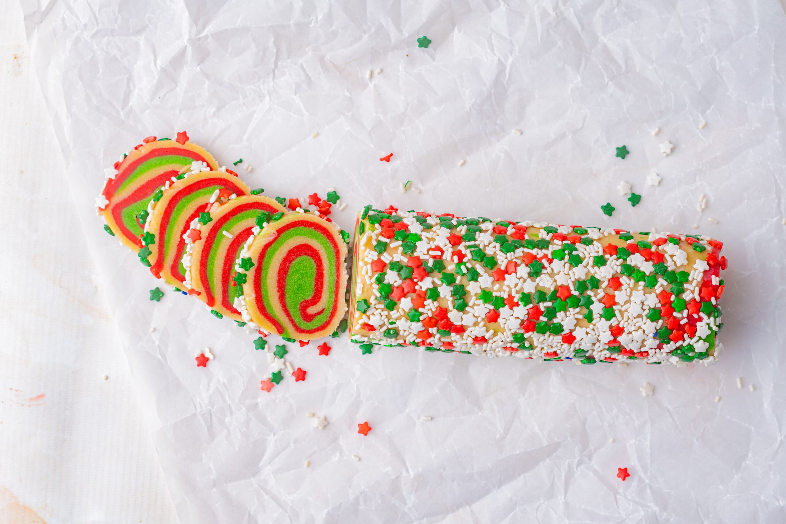 Peppermint pinwheel cookies swirl with festive red, green, and white sprinkles, creating colorful spiral treats displayed on parchment paper.