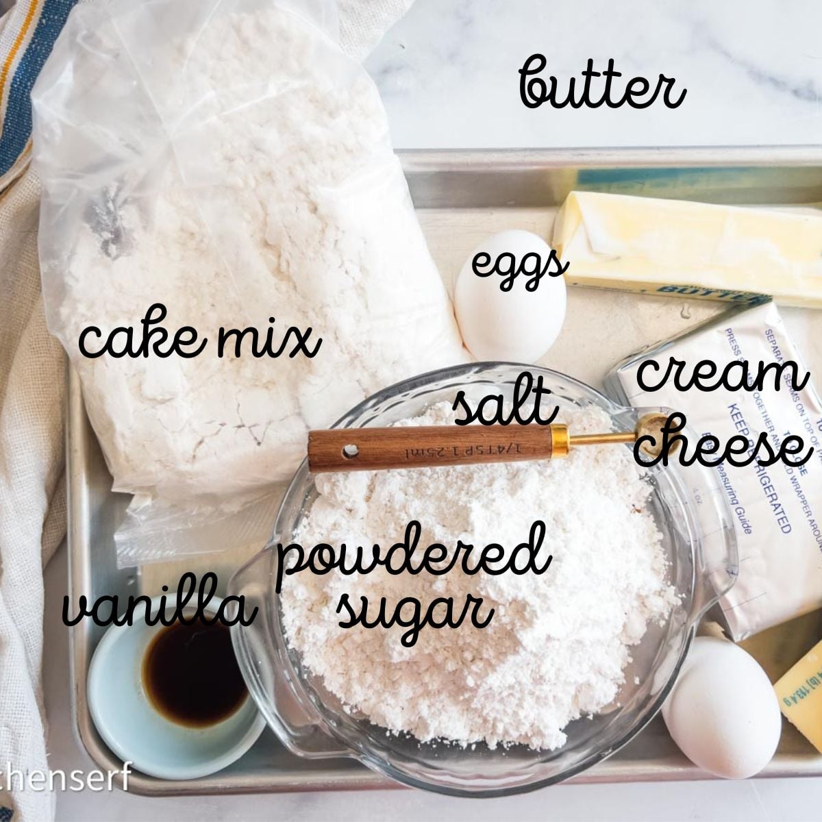 Baking ingredients on a tray for St. Louis gooey butter cake, labeled: cake mix, vanilla, eggs, butter, salt, cream cheese, powdered sugar.