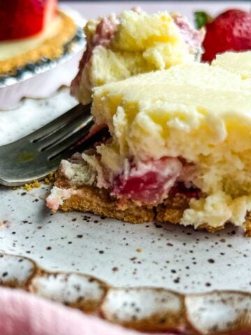 A fork cuts into a creamy strawberry cheesecake pie slice on a decorative plate, with strawberries in the background.