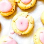 lemon cookies with raspberry icing in the middle on a parchment paper.