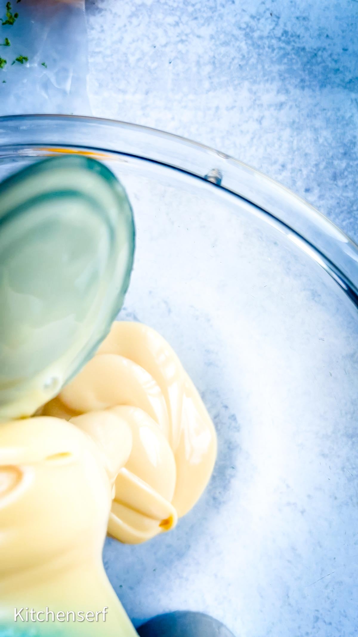 Spoon spreading sweetened condensed milk in a clear glass bowl on a light blue surface, perfect for preparing the creamy base of your favorite Nellie & Joe's Key Lime Pie.