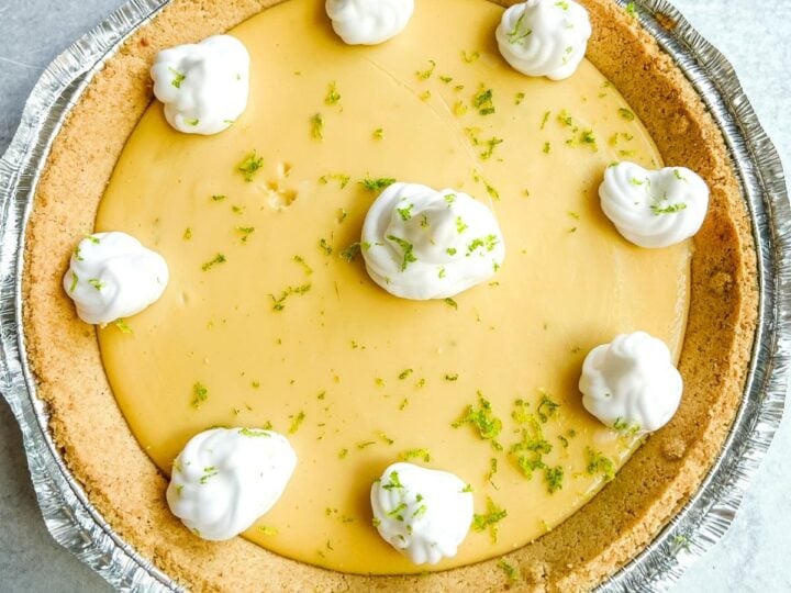 Key lime pie in a graham crust, made with Nellie & Joe's Key Lime Pie recipe, topped with whipped cream and lime zest, on a light surface.