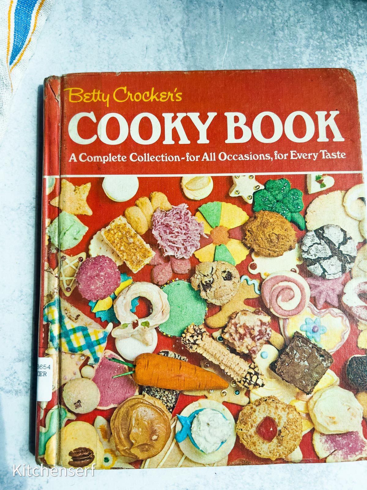 Betty Crocker's Cooky Book, one of the most beloved baking books, features colorful cookies pictured on the cover and lies on a light gray surface.