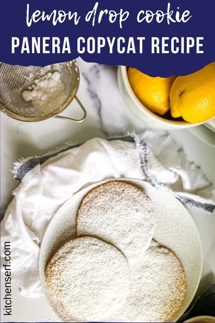 Llemon drop cookies dusted with powdered sugar on white parchment paper, with fresh lemons and a flour sifter in background, recreating Panera's popular bakery cookie