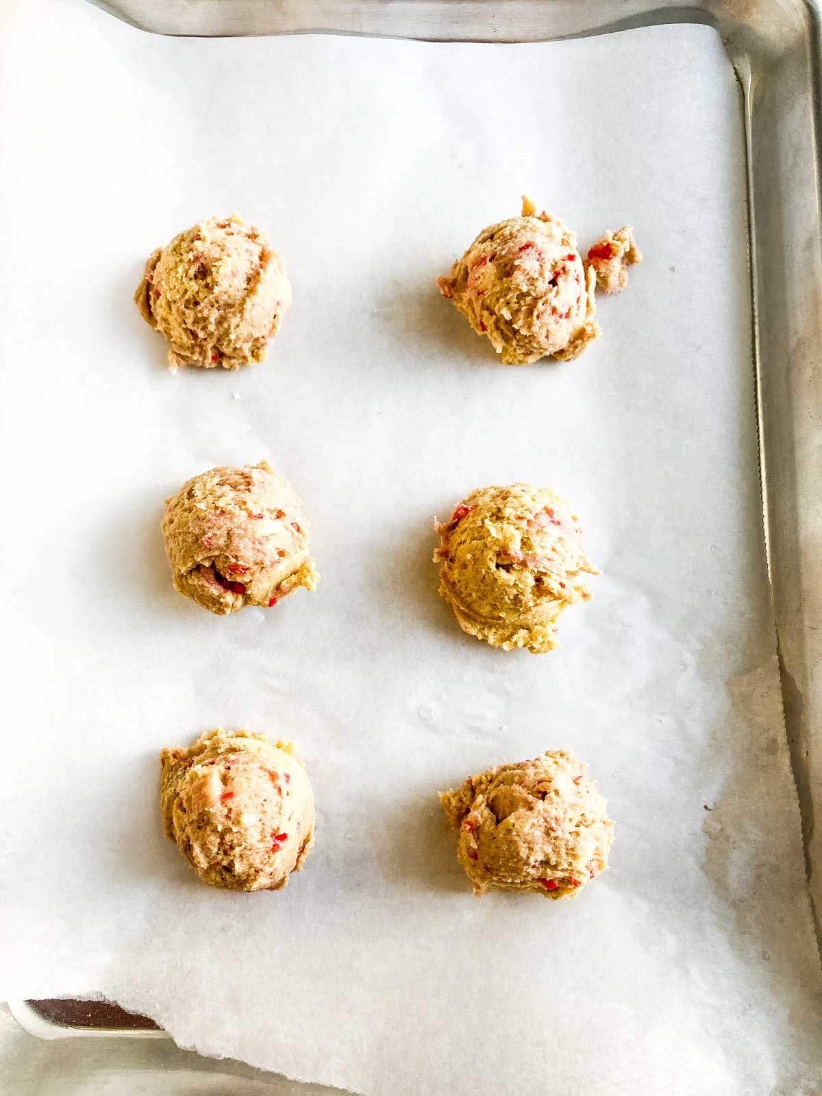 dough balls of white chocolate raspberry cookie dough on a parchment lined metal tray