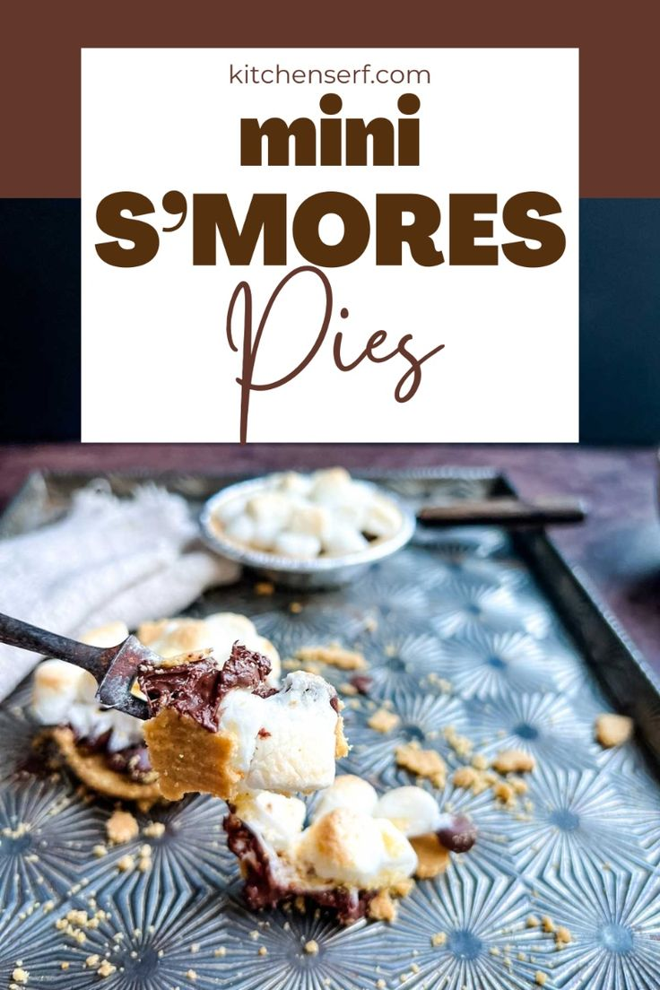 A close-up shot of a fork holding a bite of S'mores Mini Pie, showing a gooey layer of melted marshmallow and chocolate with a graham cracker crust. In the background, there is a mini pie on a baking sheet.