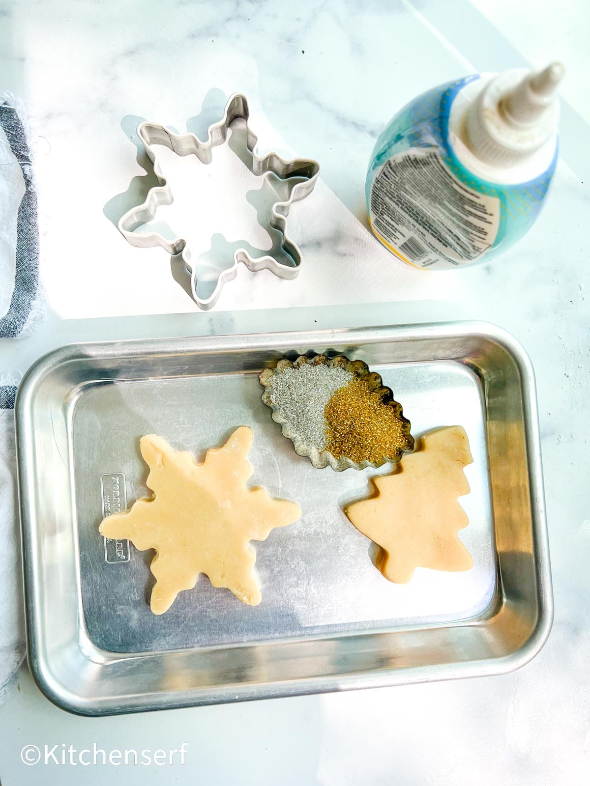 star sugar cookie cut outs on a baking sheet with cookie cutter and gold and silver sprinkles.