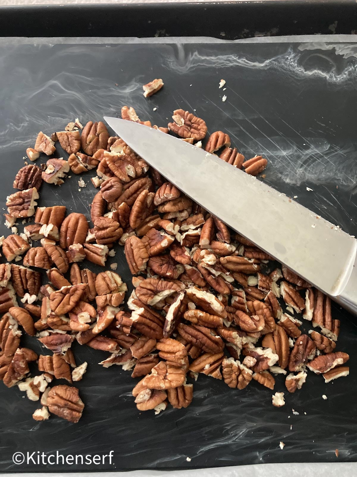 chopped pecans on a cutting board with a chef's knife.