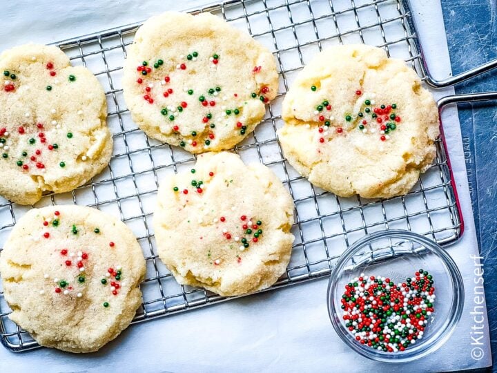 sugar cookies with sprinkles on top on a rack next to a small bowl of nonpareils.