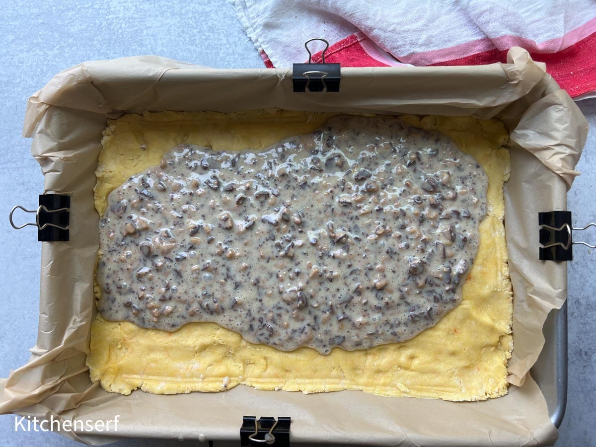 A parchment-lined pan with dough and a layer of toffee and sweetened condensed milk on top.