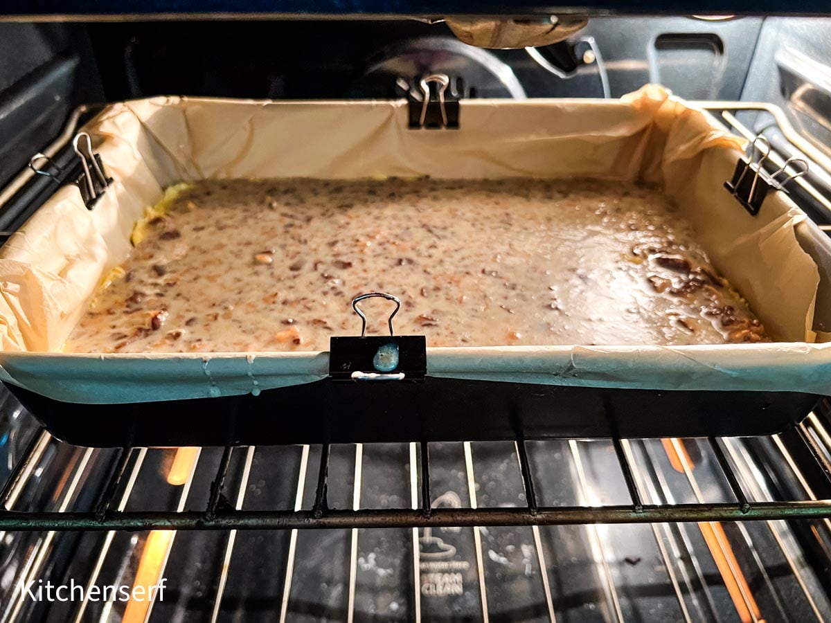 A parchment-lined pan of batter baking in an oven, secured with binder clips on the sides.