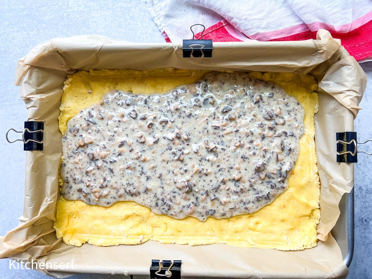 A baking pan with dough and a layer of creamy mushroom mixture, lined with parchment paper and binder clips.