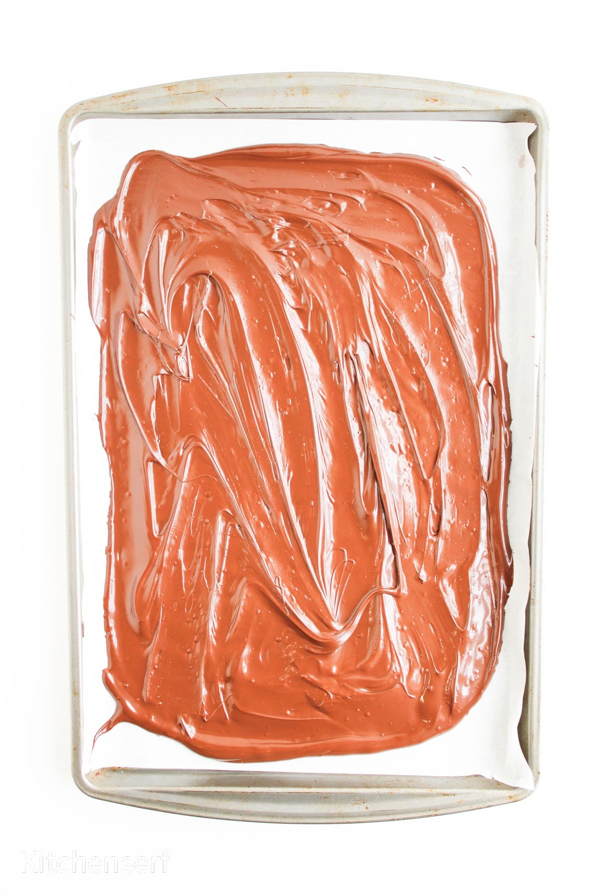 A baking sheet with parchment paper topped with swirled melted milk chocolate.