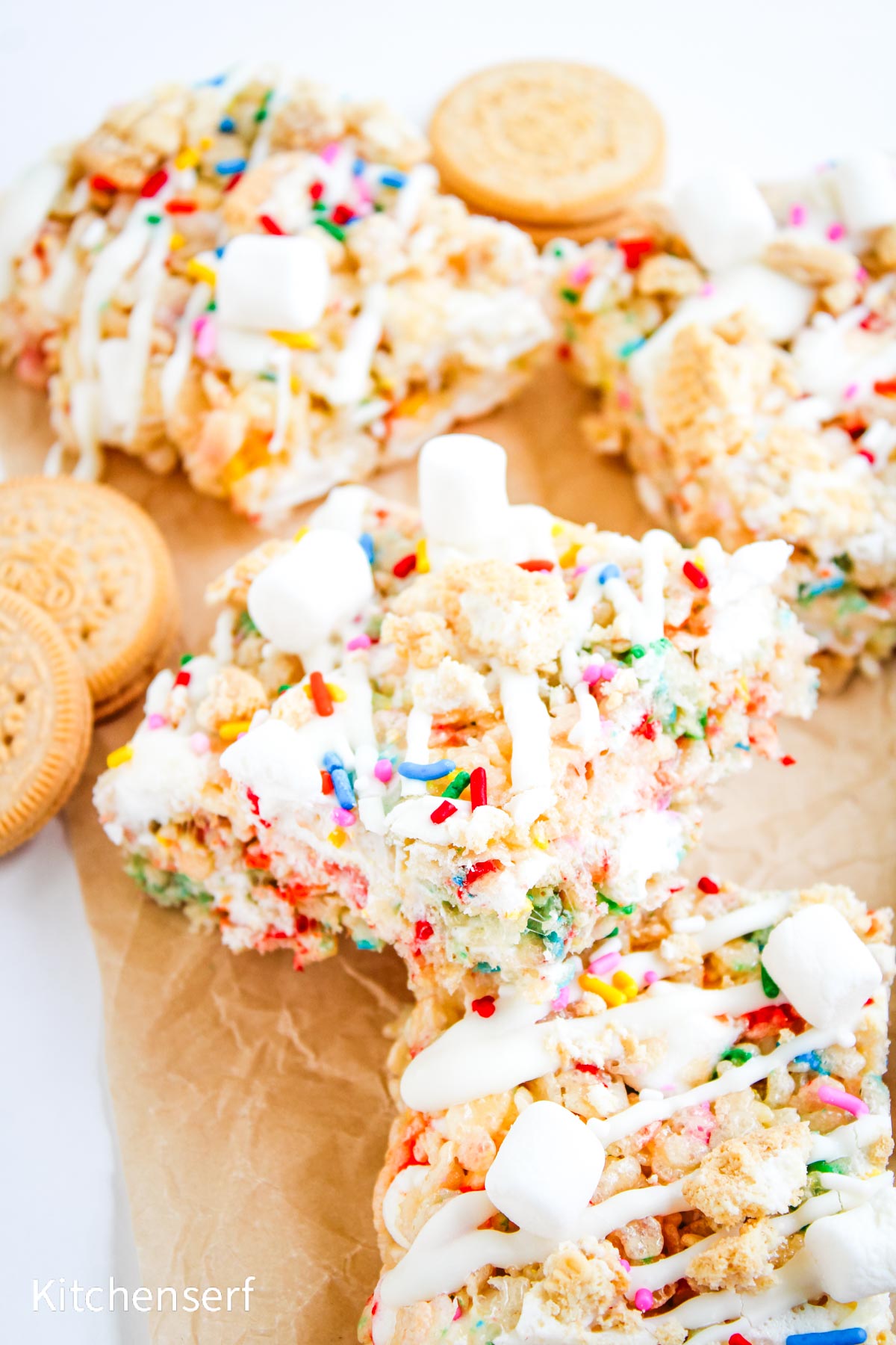 Marshmallow cereal treats with sprinkles, mini marshmallows, white drizzle, and golden sandwich cookies.