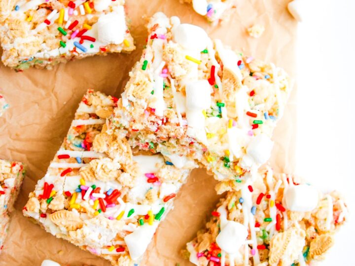 Colorful dessert bars with sprinkles, marshmallows, and cookie pieces on parchment paper, stacked together.