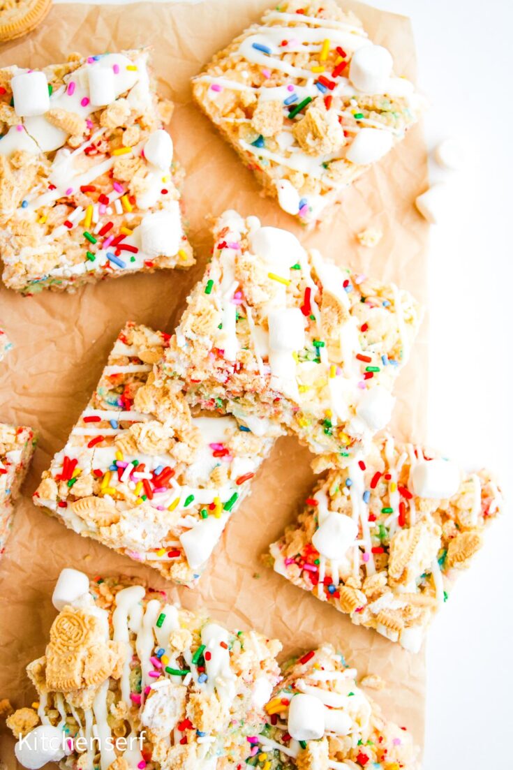 Colorful dessert bars with sprinkles, marshmallows, and cookie pieces on parchment paper, stacked together.