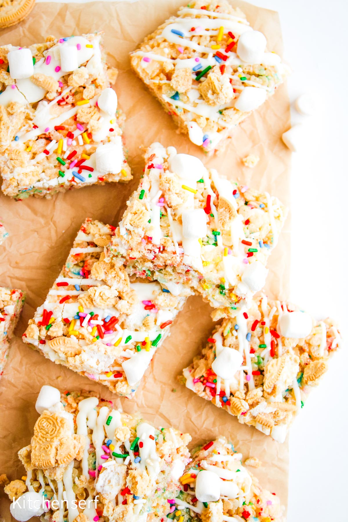 Colorful dessert bars with sprinkles, marshmallows, and cookie pieces on parchment paper, stacked together.