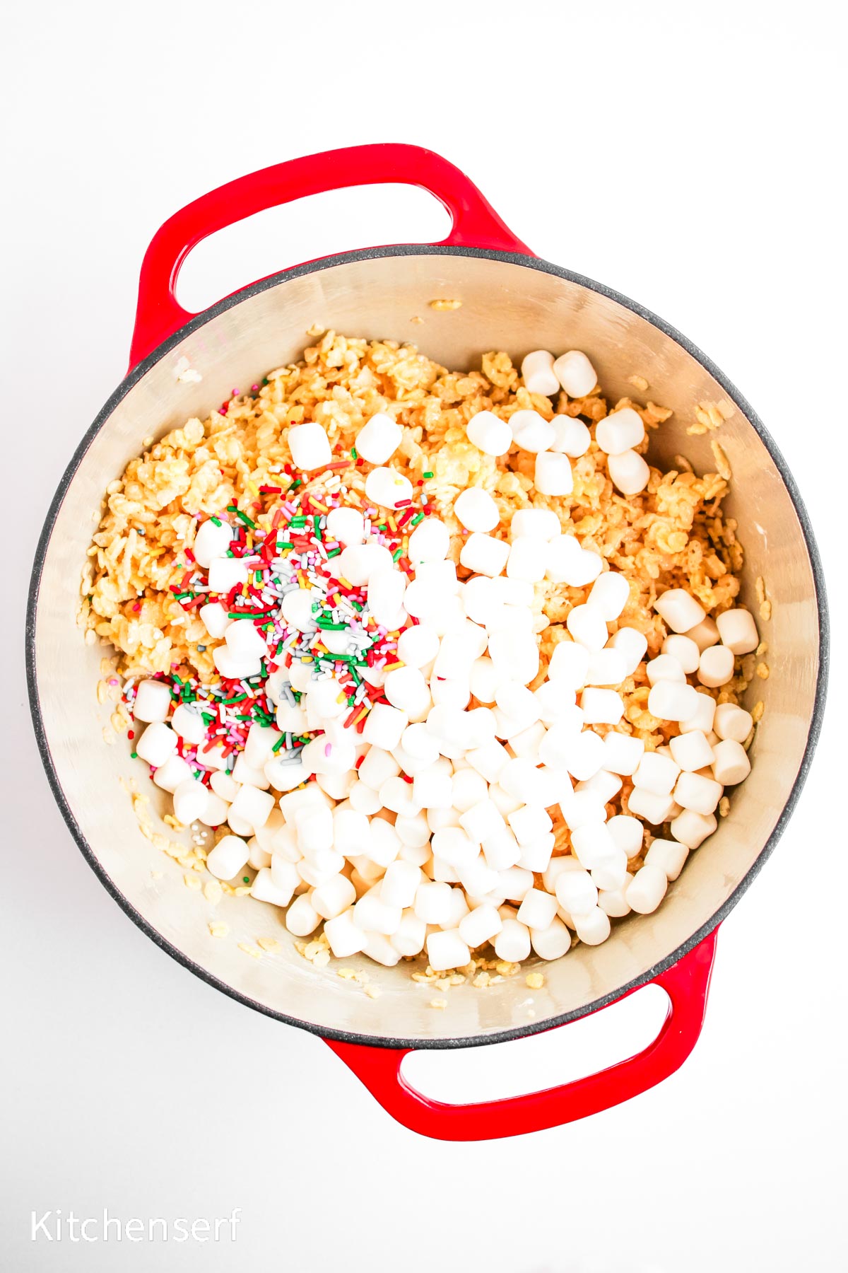 Large red pot with rice cereal, mini marshmallows, and colorful sprinkles on a white background.