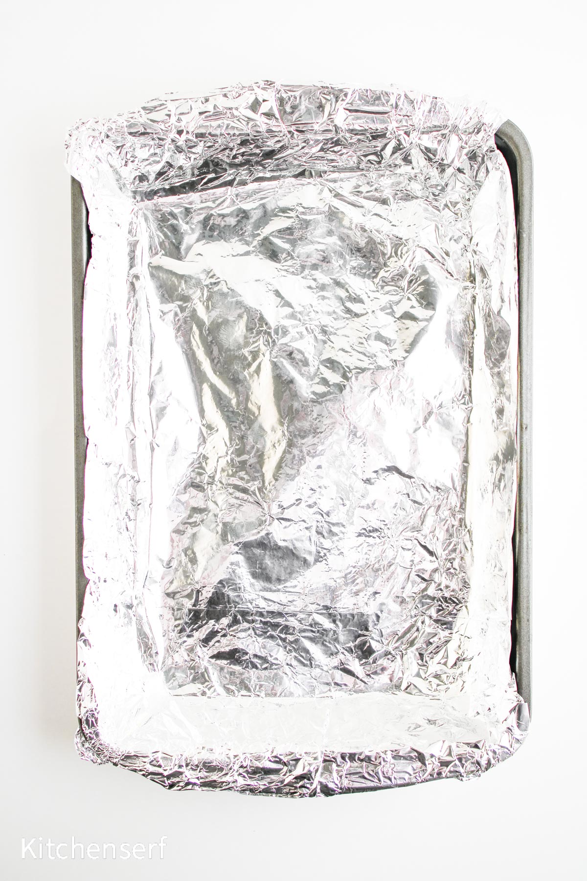 A baking sheet lined with crinkled aluminum foil on a white background.