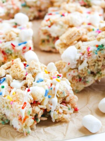 Colorful rice krispie treats with sprinkles, cereal pieces, and mini marshmallows on parchment paper.