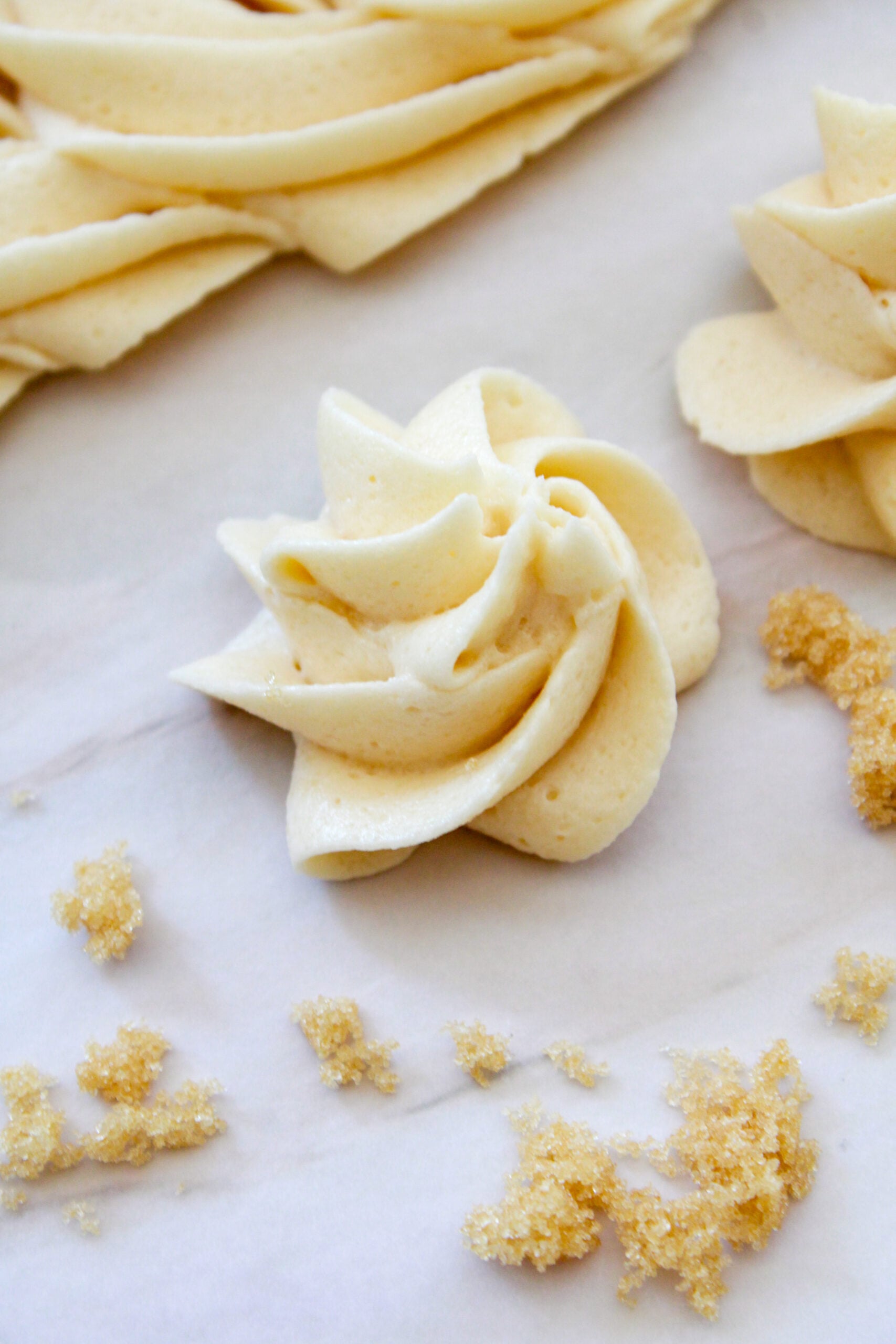 Swirl of vanilla frosting on parchment paper with scattered brown sugar crystals nearby.