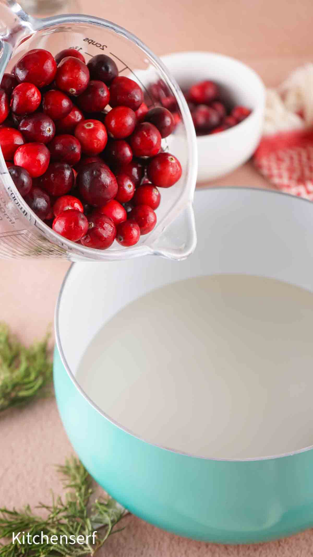 Fresh cranberries being poured from a glass measuring cup into a large pot filled with water.