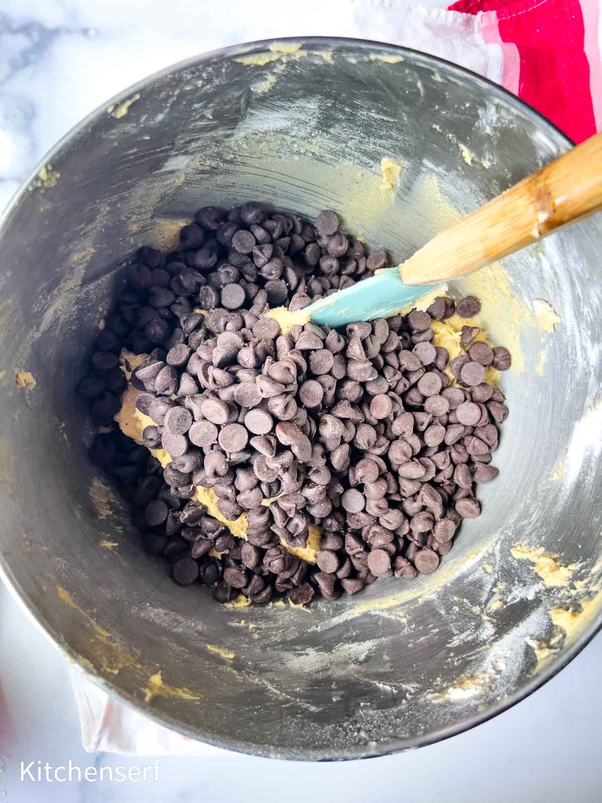 A mixing bowl with cookie dough and chocolate chips, being stirred with a spatula.