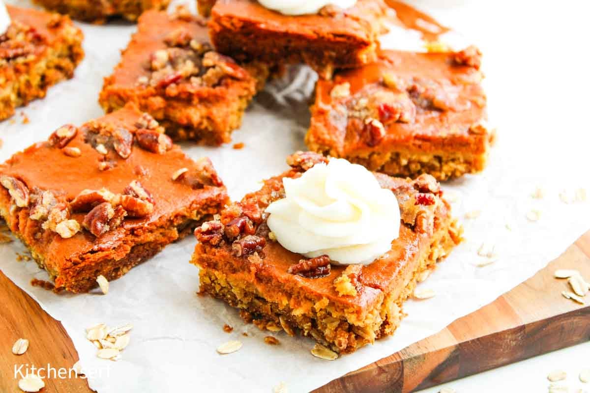 Pumpkin pecan pie bars with a frosting swirl on top, arranged on a wooden board lined with parchment paper.