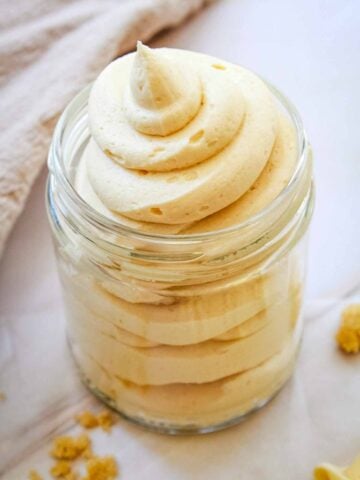 brown sugar frosting piped into a small glass jar on a marble counter.