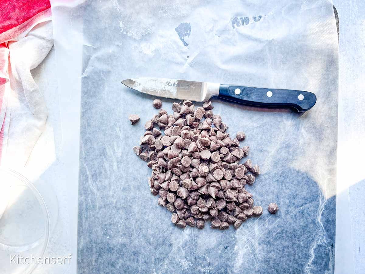 Chocolate chips on a sheet of wax paper next to a black-handled knife.