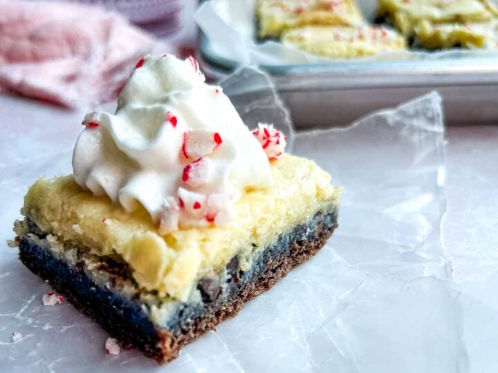 chocolate dessert square with cream cheese layer topped with whipped cream sprinkled with peppermint candy shards.