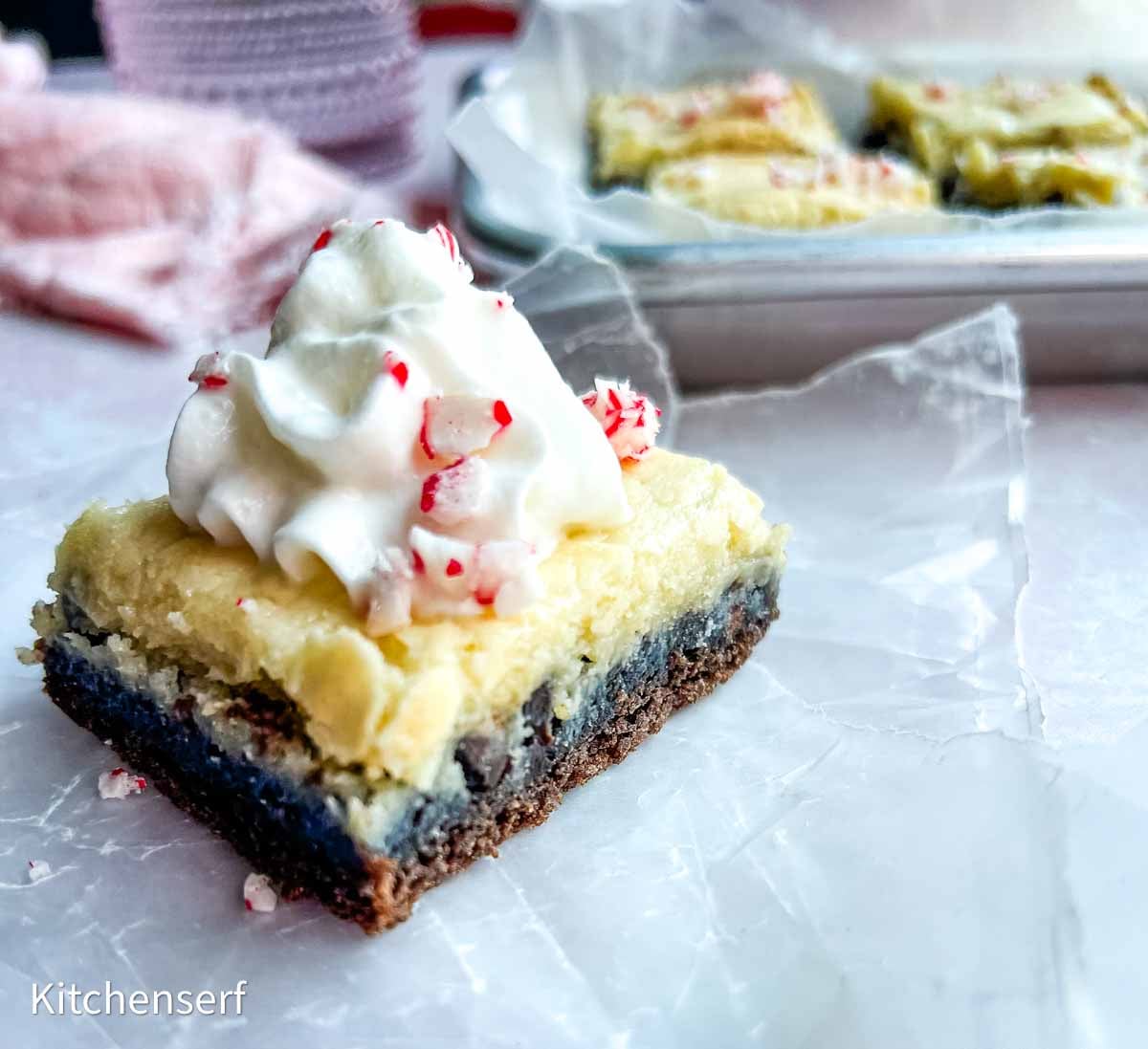 chocolate dessert square with cream cheese layer topped with whipped cream sprinkled with peppermint candy shards.