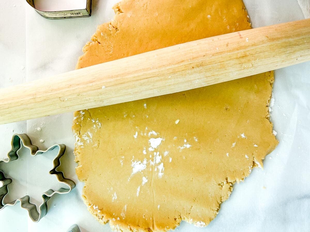 sugar cookie dough on a piece of parchment with a wooden rolling pin on top next to a snowflake cookie cutter.