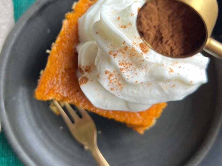 slice of pumpkin gooey butter cake on black plate with gold fork and spice being sprinkled on top.