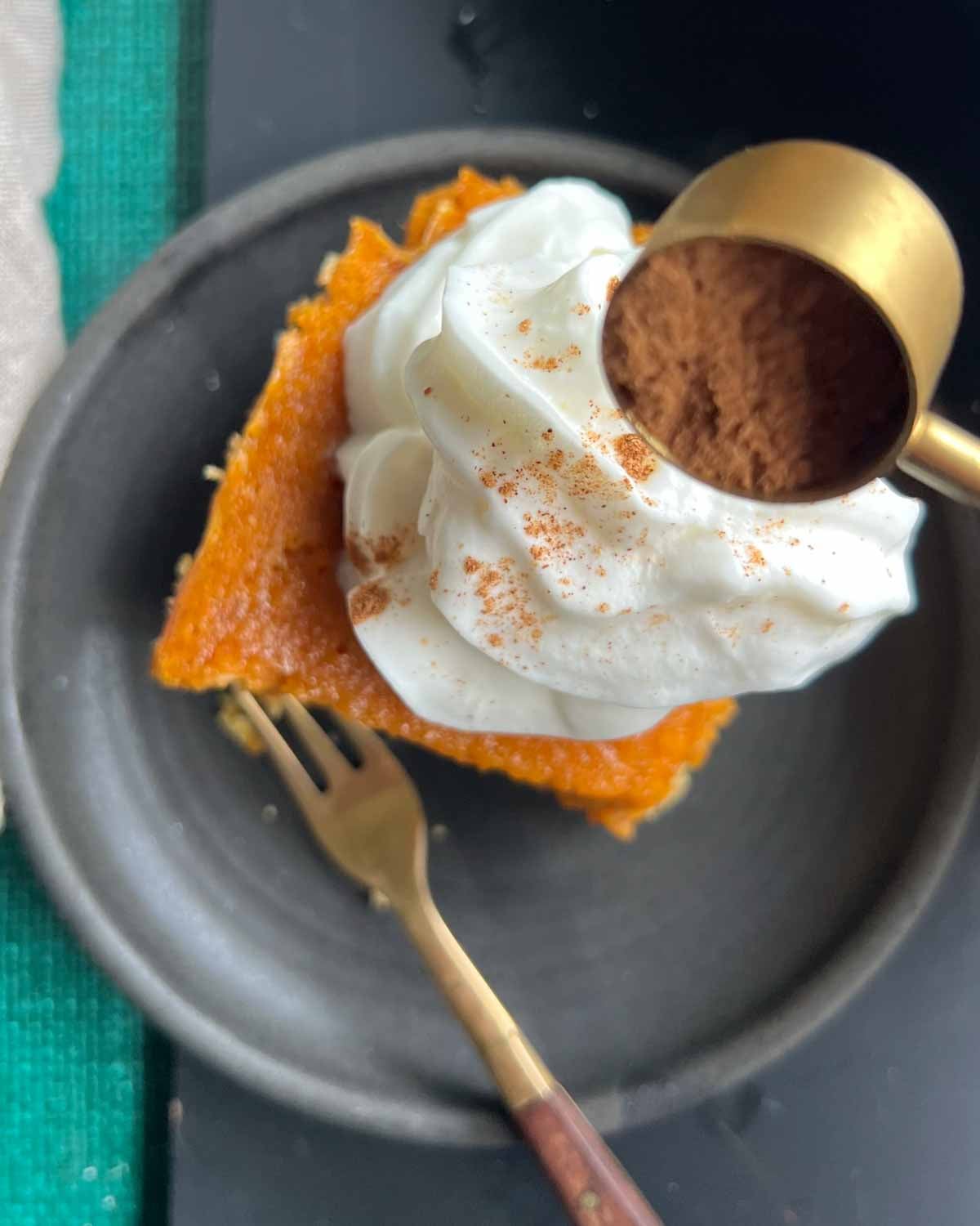 slice of pumpkin gooey butter cake on black plate with gold fork and spice being sprinkled on top.