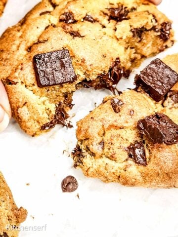 Close-up of an air fryer chocolate chip cookie broken in half, revealing melted chocolate chunks and a soft center.