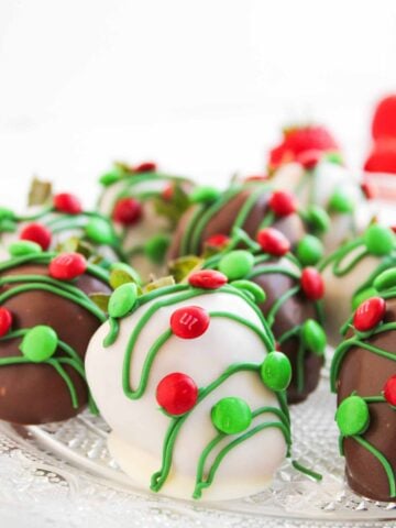 Chocolate and white chocolate-covered strawberries decorated with green icing and red candy on a glass plate.