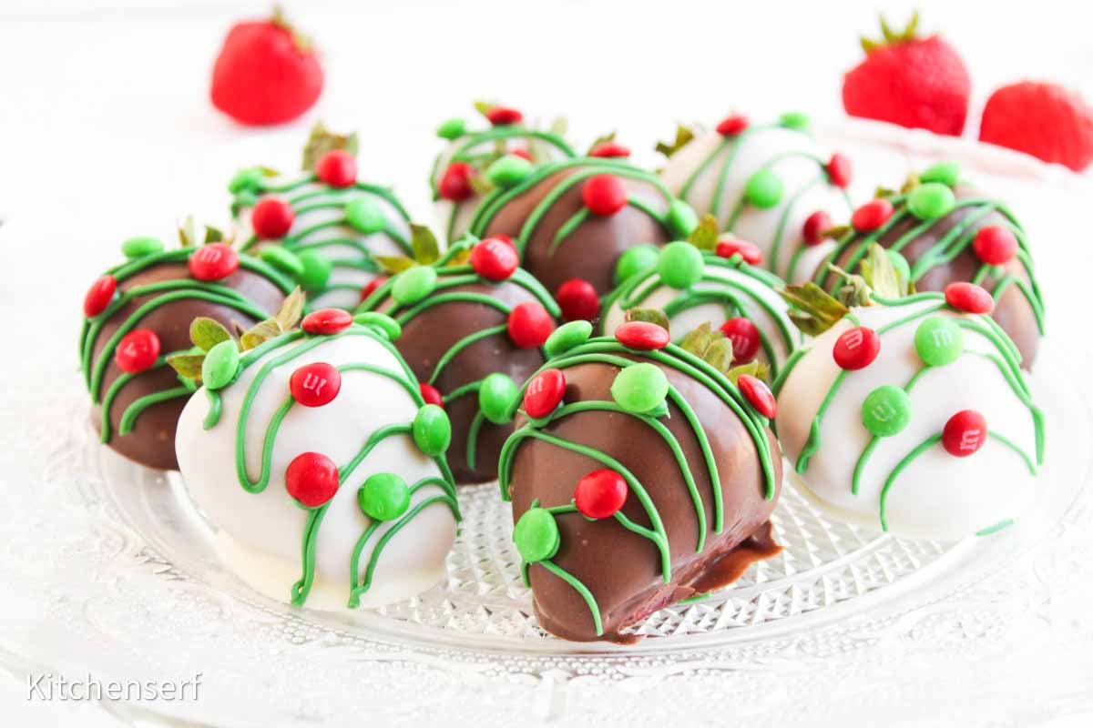 Chocolate-covered strawberries decorated with red and green candy and icing, arranged on a glass plate.