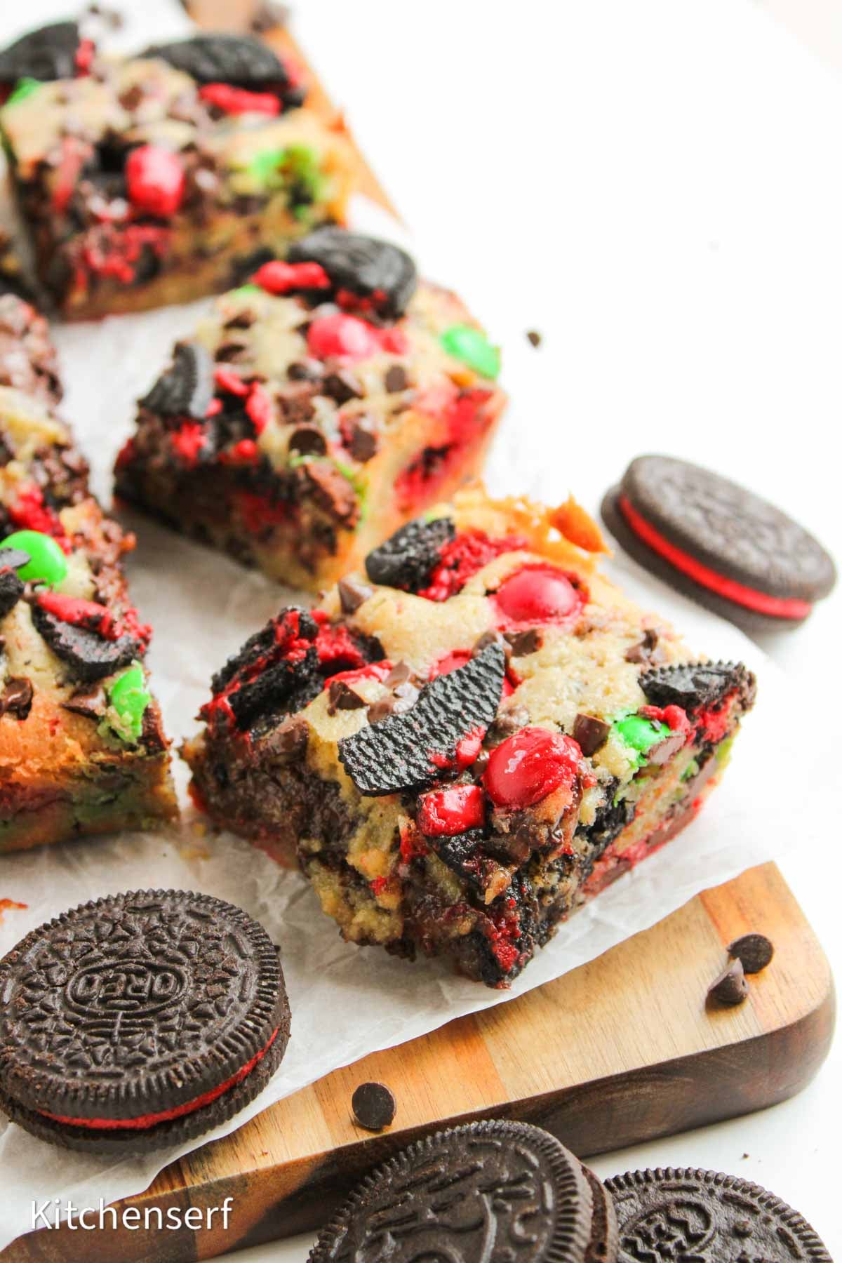 Colorful cookie bars with Oreo cookies and red and green candies, cut into squares on a wooden board.