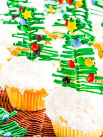 Christmas Tree Cupcakes topped with white frosting and decorated with green candy Christmas trees and colorful candy ornaments.
