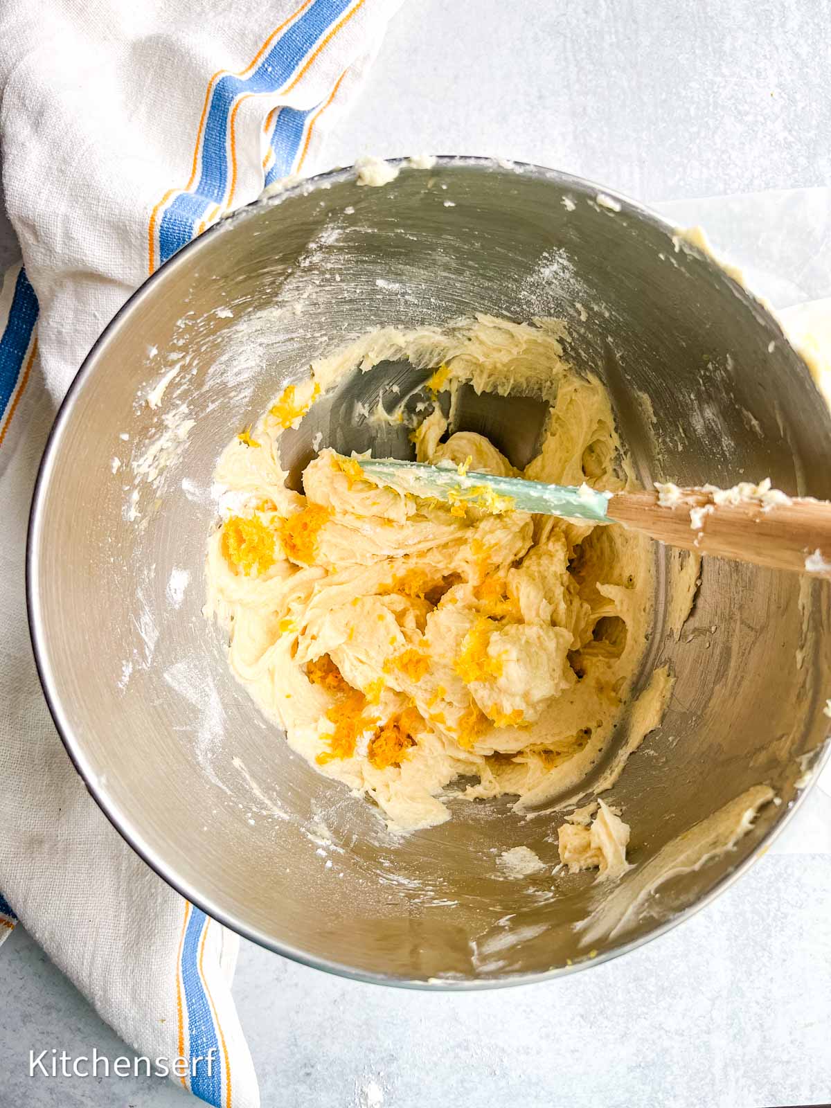 Mixing bowl with cookie dough and orange zest, a spatula, and a striped towel beside the bowl.