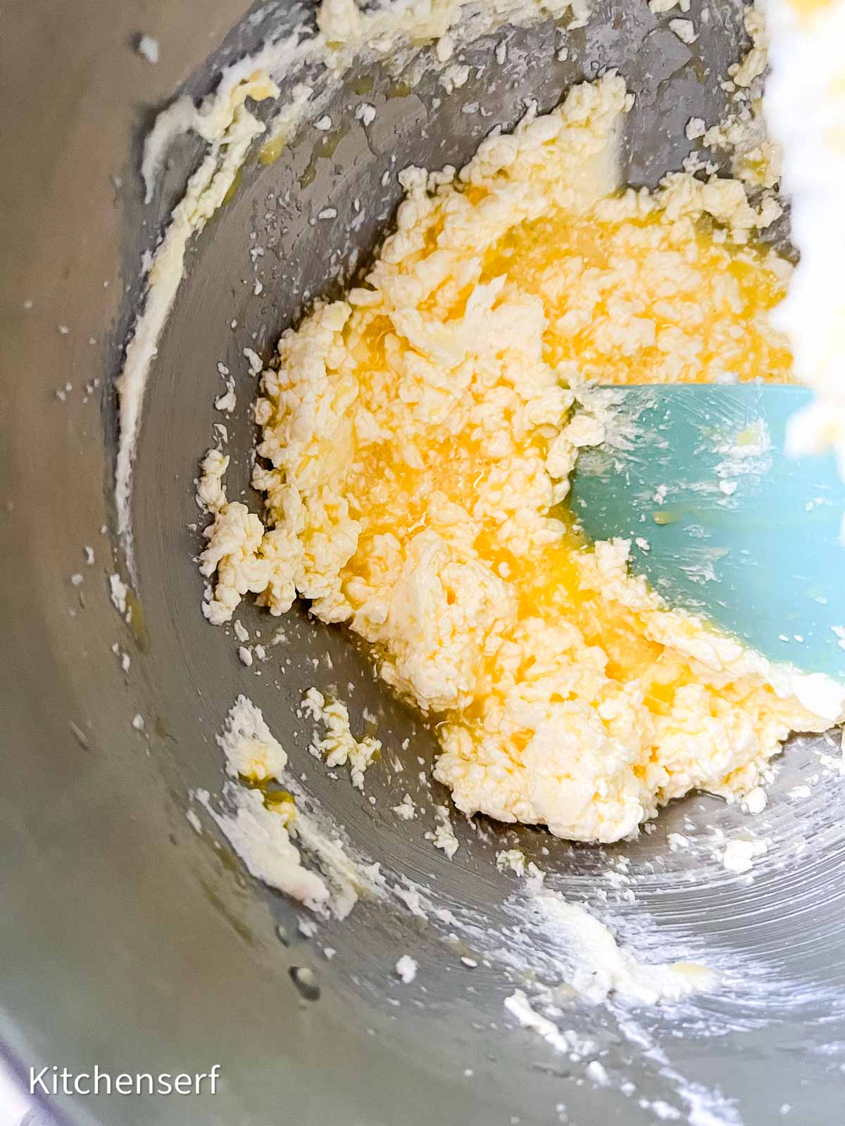 Butter and sugar being creamed together in a mixing bowl with a blue spatula.