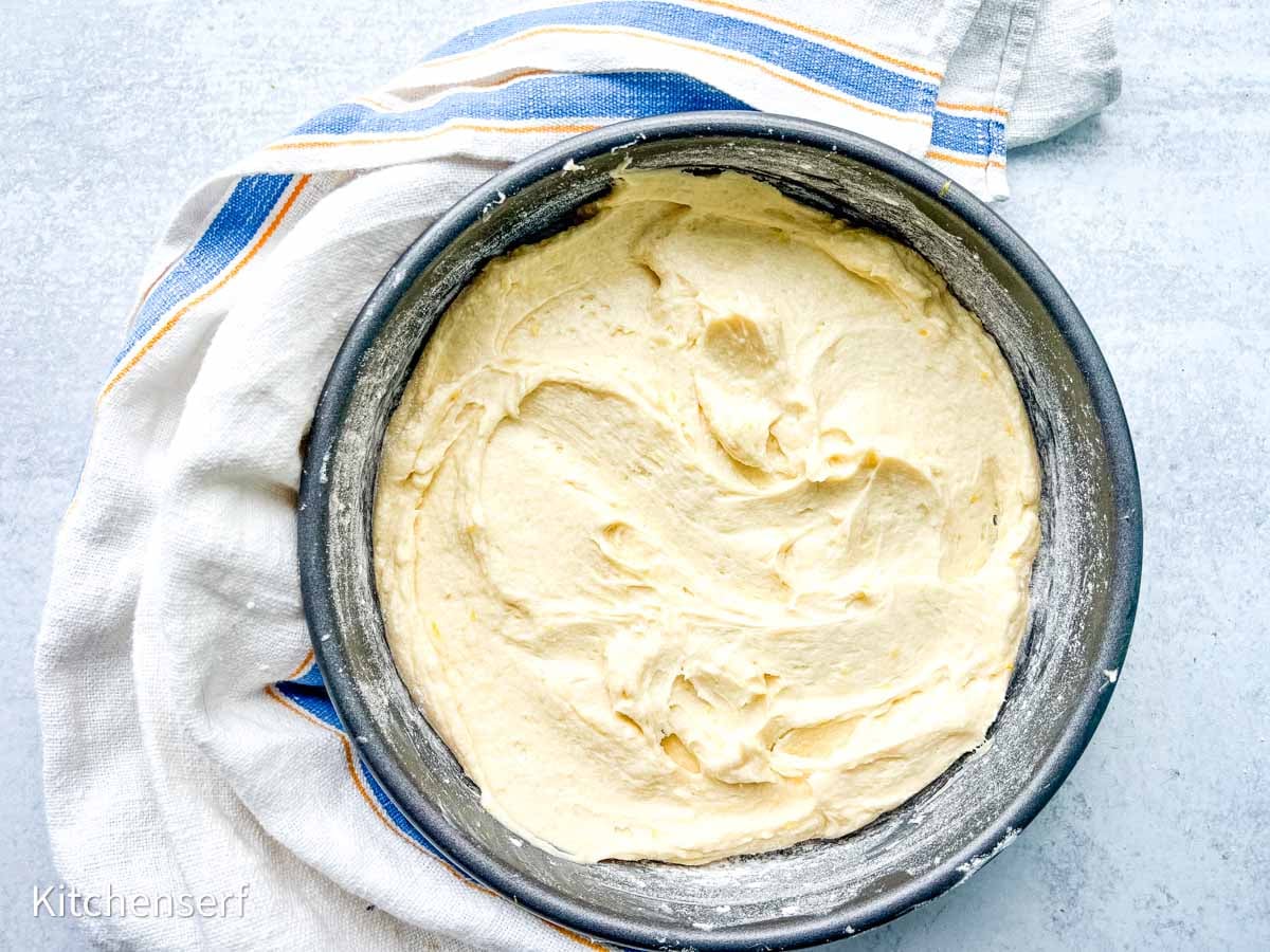 Cake batter spread in a round pan, resting on a striped kitchen towel on a light surface.
