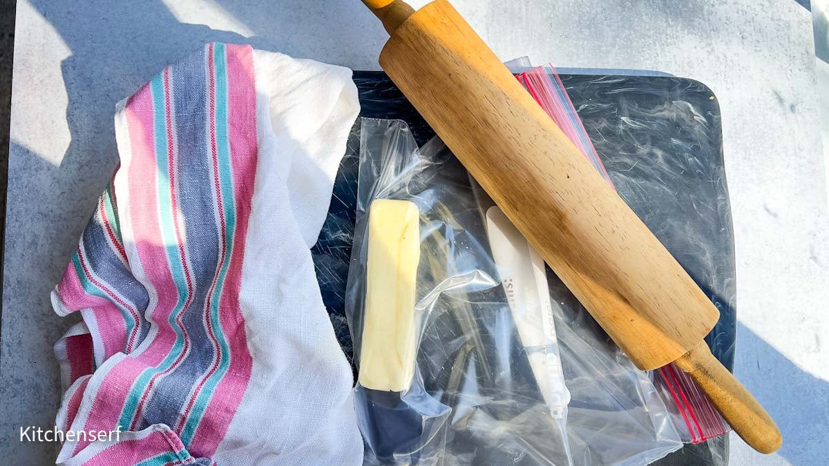 Rolling pin, butter stick, plastic bags, knife, and striped towel on a black marble cutting board.